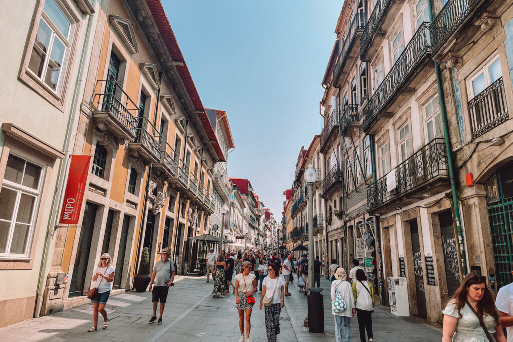 Busy Rua das Flores in Porto, lined with historic buildings and boutique shops, filled with people walking and shopping – a must-stroll pedestrian street on a 2-day Porto itinerary.