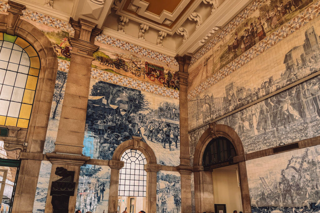 Interior of São Bento Railway Station in Porto, featuring large azulejo tile murals depicting historical Portuguese scenes – a cultural highlight to explore in Porto.