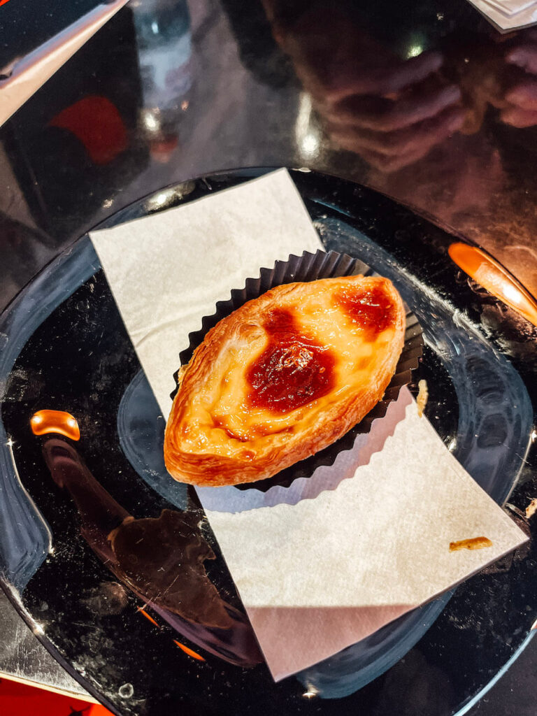 A single pastel de nata tart on a black plate with a crispy, golden crust and custard centre – a must-try pastry during your 2 days in Porto.