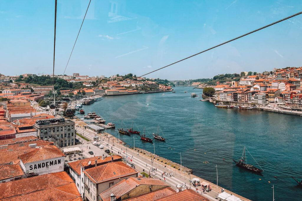 Aerial view of the Douro River from the Vila Nova de Gaia cable car, with traditional boats and Porto’s waterfront buildings in sight – a scenic experience to enjoy in Porto.