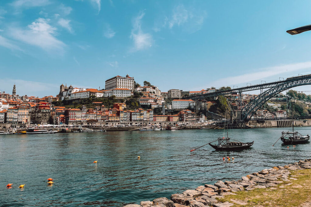 Colourful Ribeira district buildings and Porto Cathedral seen from across the Douro River, with Rabelo boats floating in the foreground – a postcard view perfect for your Porto itinerary.