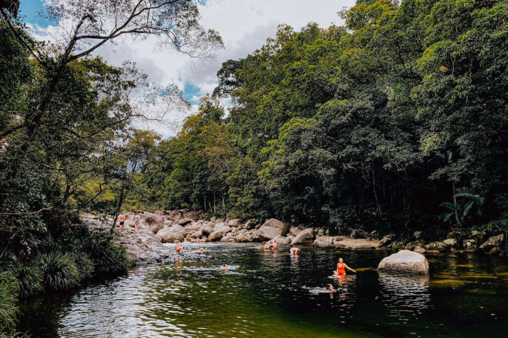 People swimming in a clear, tropical river surrounded by lush greenery in the Daintree Rainforest – a must-visit stop on a 2-week Australia itinerary through Far North Queensland.
