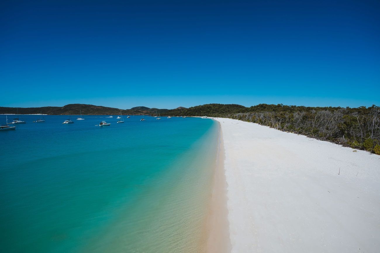 Turquoise water and white sand at Whitehaven Beach in the Whitsundays, one of the highlights of a 3 weeks in Australia itinerary, with yachts anchored offshore under a bright blue sky.