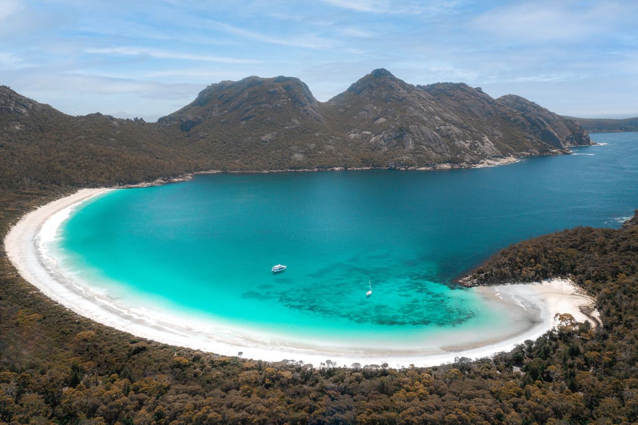A stunning view of Wineglass Bay in Freycinet National Park, Tasmania — a must-see stop on any 4 weeks in Australia trip. This Australia itinerary highlight features a perfect crescent of white sand, turquoise water, and rugged granite mountains, with boats anchored in the bay.