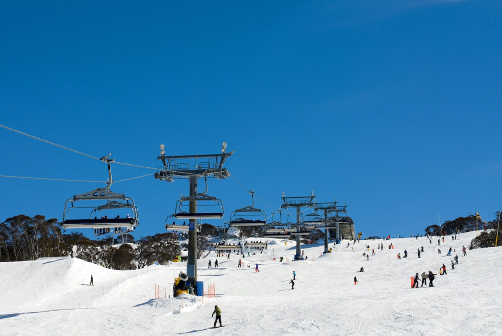 Snowboarders and skiers enjoying the slopes under a bright blue sky at Perisher ski resort in New South Wales — showing why winter is one of the best times to visit Australia for snow sports and alpine adventures.
