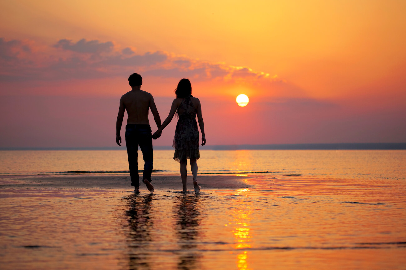 Romantic couple walking hand-in-hand into the ocean at sunset, the perfect moment for a honeymoon in Australia.