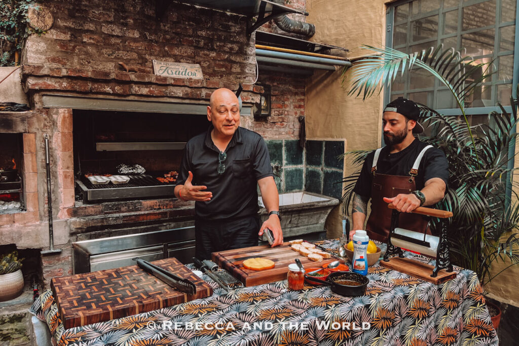 Host explaining the cooking process beside a traditional parrilla during the Asado Adventure asado experience in Buenos Aires, showcasing authentic Argentine barbecue techniques.