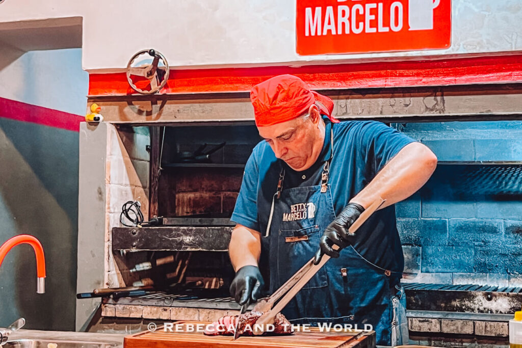 A chef at Betty and Marcelo Buenos Aires slices grilled meat on a wooden board using tongs and a knife, demonstrating preparation during a traditional family asado in Buenos Aires.