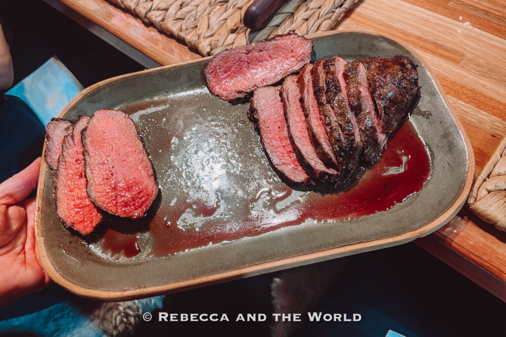 A platter of sliced steak with a pink center and meat juices pooling on the plate, served during the Buenos Aires asado experience at Betty and Marcelo Buenos Aires.