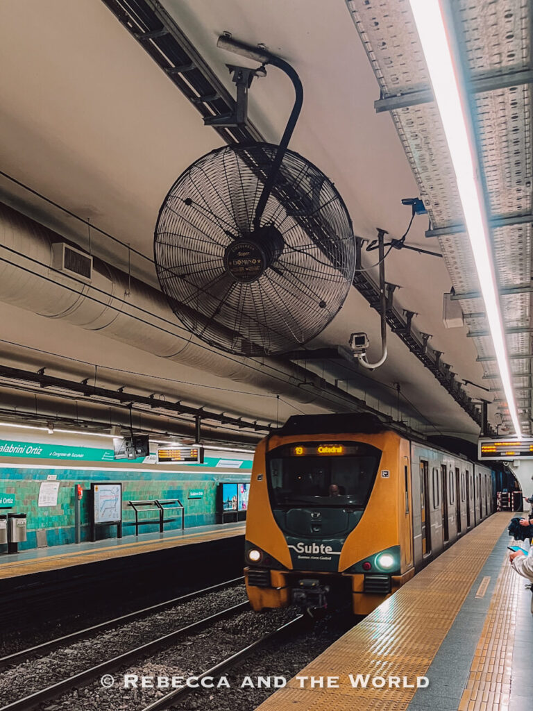 A yellow subway train arrives at an underground station, with passengers waiting on the platform. Public transport like the Buenos Aires Subte is an affordable way to get around Buenos Aires on a budget.