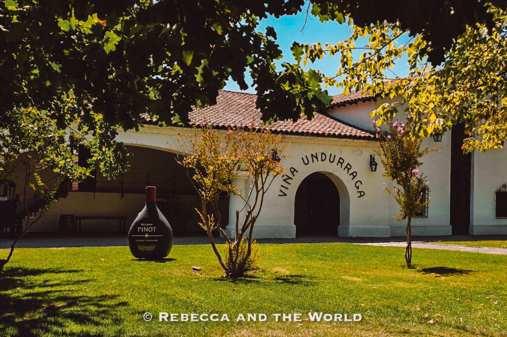 A white building with an arched entrance labeled “Viña Undurraga” stands behind a green lawn and trees, a popular stop on a Maipo Valley tour for wine tastings and history.