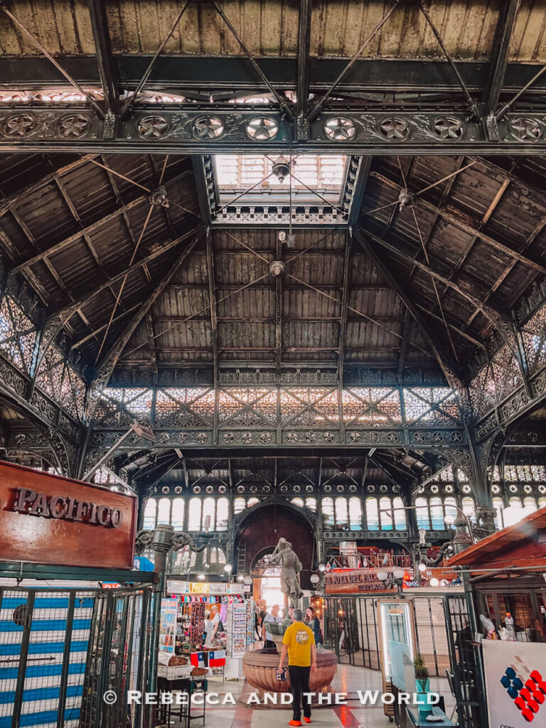 Interior of a bustling Santiago market hall with ornate iron architecture and small food stalls, a vibrant setting for a Santiago walking food tour focused on traditional Chilean food.
