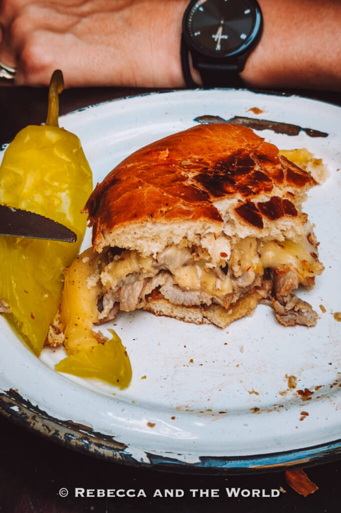 Close-up of a Chilean sandwich with melted cheese and meat alongside a pickled pepper, a popular street food featured on a Santiago walking food tour and part of what to eat in Chile.