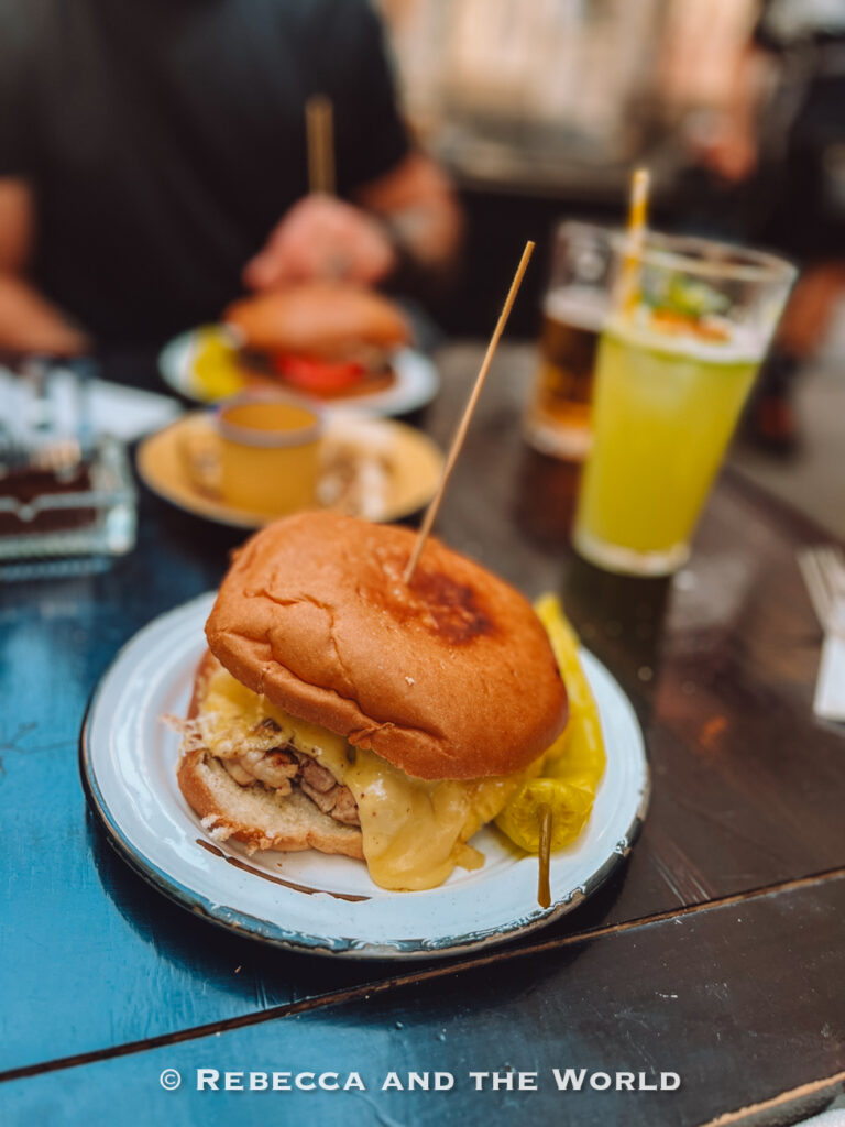 Close-up of a Chilean sandwich with melted cheese and meat alongside a pickled pepper, a popular street food featured on a Santiago walking food tour and part of what to eat in Chile.