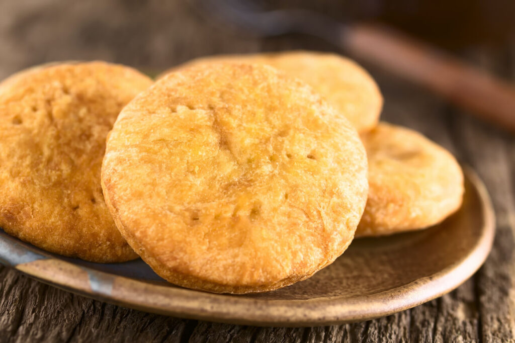 Close-up of golden, round sopaipillas (traditional Chilean fried bread) on a rustic plate, a classic example of traditional Chilean food often featured on a Santiago food tour or when exploring what to eat in Chile.