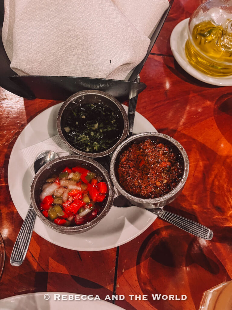 Three small bowls of sauces, including chimichurri, salsa criolla and provencal, arranged on a plate as condiments during a Buenos Aires food tou.