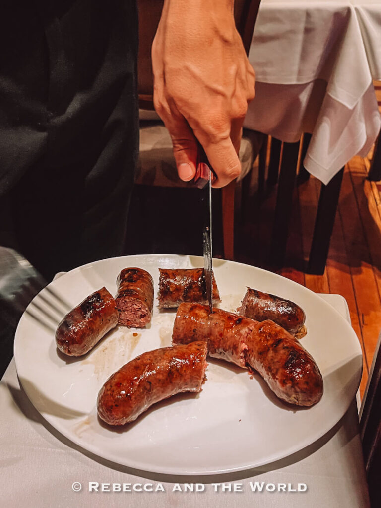 A server cutting grilled chorizo into pieces on a white plate, showing a traditional dish sampled during the best food tour in Buenos Aires.