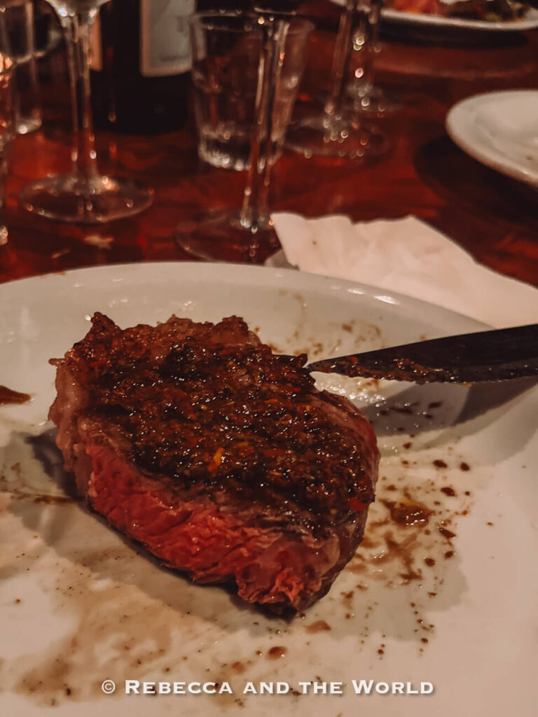 Close-up of a cooked steak on a plate with juices and seasoning, partially cut, highlighting a savory dish enjoyed on a food tour in Buenos Aires.
