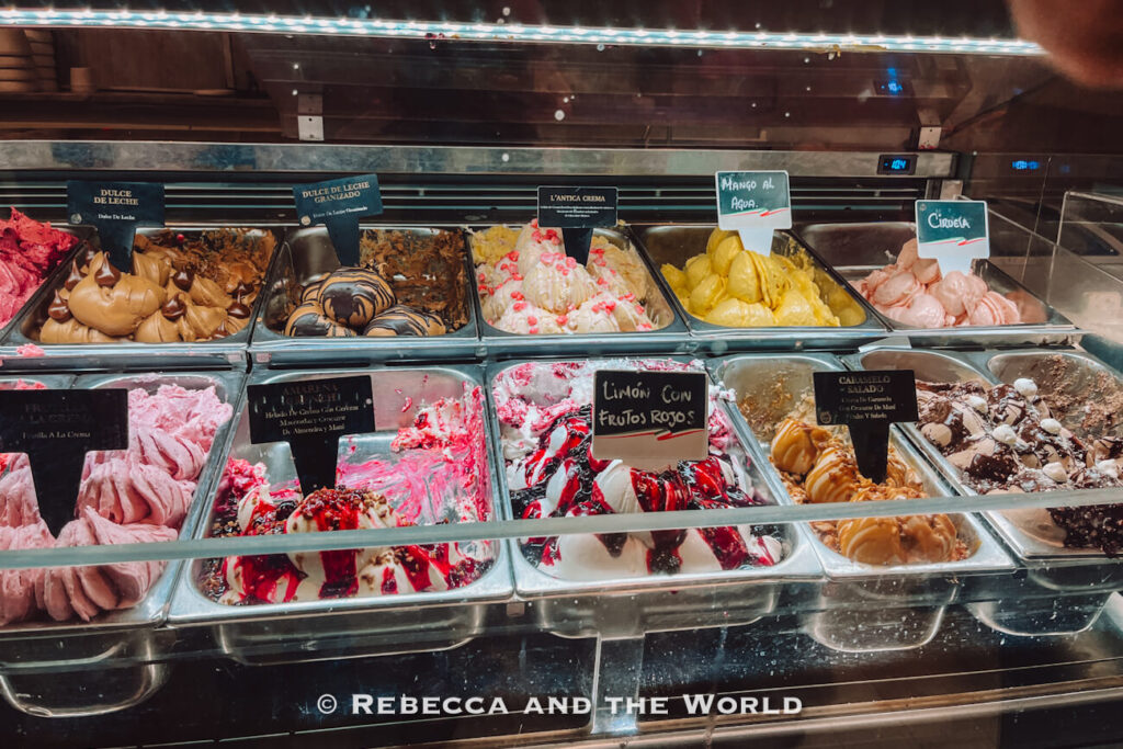 A gelato display case filled with various flavors labeled in Spanish, including dulce de leche and fruit options, showcasing a dessert stop on the best food tour in Buenos Aires.