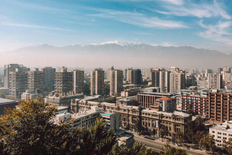 A wide view of Santiago’s skyline with mid-rise buildings in the foreground and the Andes mountains rising in the background under a hazy sky—capturing a panoramic perspective of Santiago top attractions and the city’s natural setting.