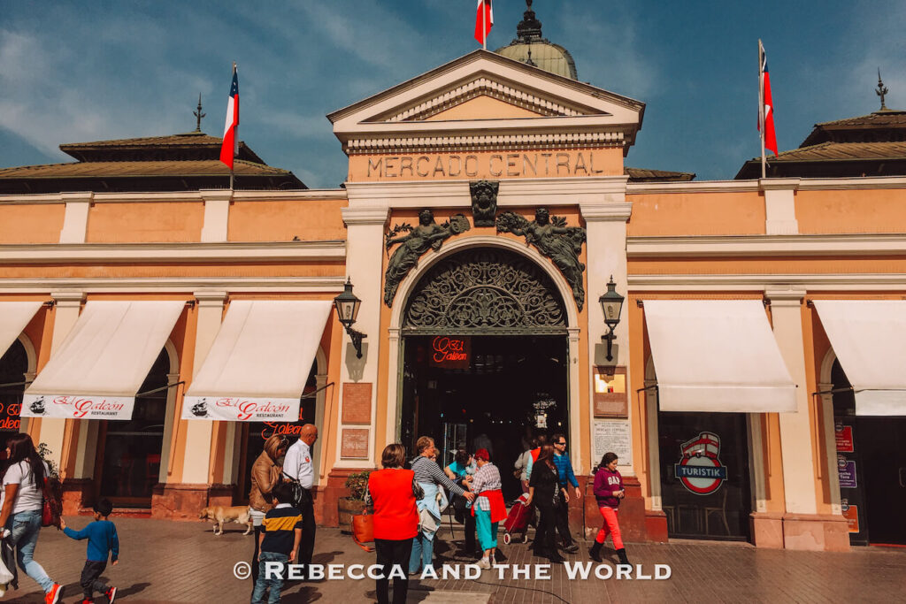 The entrance of Mercado Central with its yellow facade, Chilean flags, and people walking in and out—highlighting a bustling market and popular choice for what to do in Santiago.