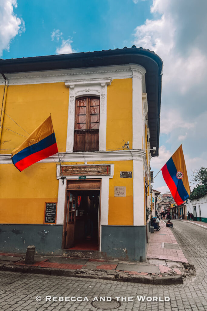 Bright yellow colonial corner building displaying Colombian flags along a cobblestone street in La Candelaria, one of the best places to visit in a 2-day Bogotá itinerary.