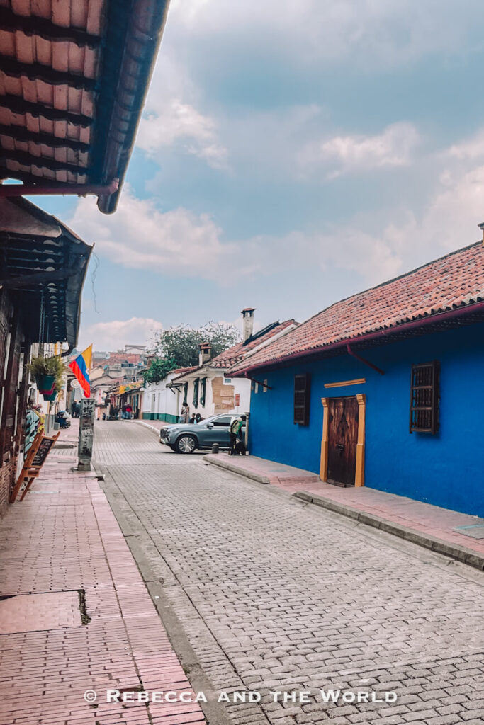 Quiet cobblestone street lined with colorful colonial buildings, including a bright blue house, in Bogotá’s historic La Candelaria district, showing what to do in Bogotá.