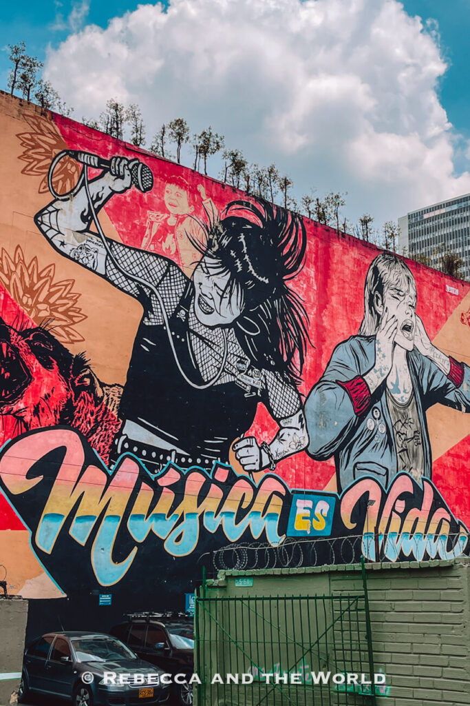 Massive red street art mural featuring illustrated musicians and the words “Música es Todo” painted on a city wall in Bogotá, a stop on many Bogotá itinerary routes.