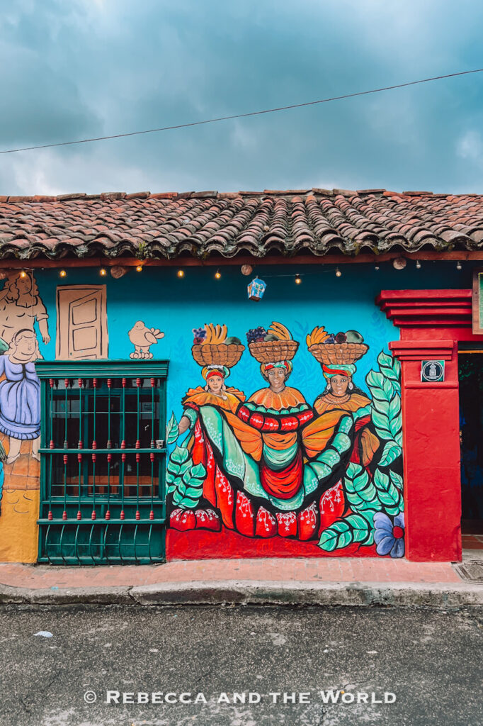 Vibrant mural of three women carrying baskets of fruit painted on the exterior wall of a colorful colonial building in Bogotá, highlighting local culture in a Bogotá travel guide.