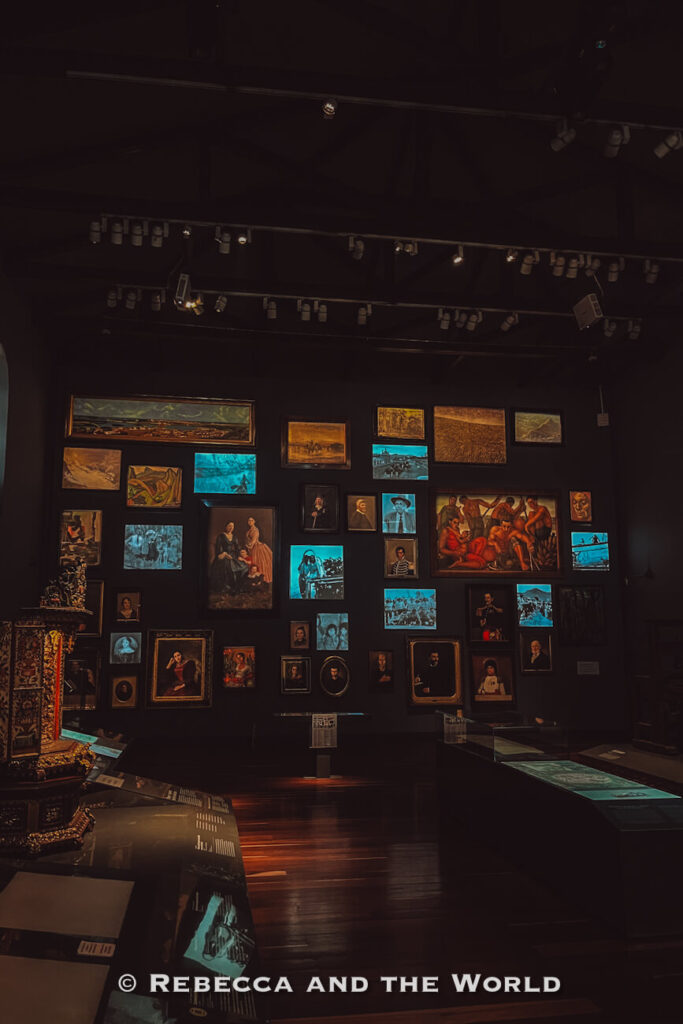 Dimly lit museum gallery in the Museo Nacional de Colombia displaying framed paintings, photographs, and historical artifacts on dark walls, one of the top indoor things to do in Bogotá.