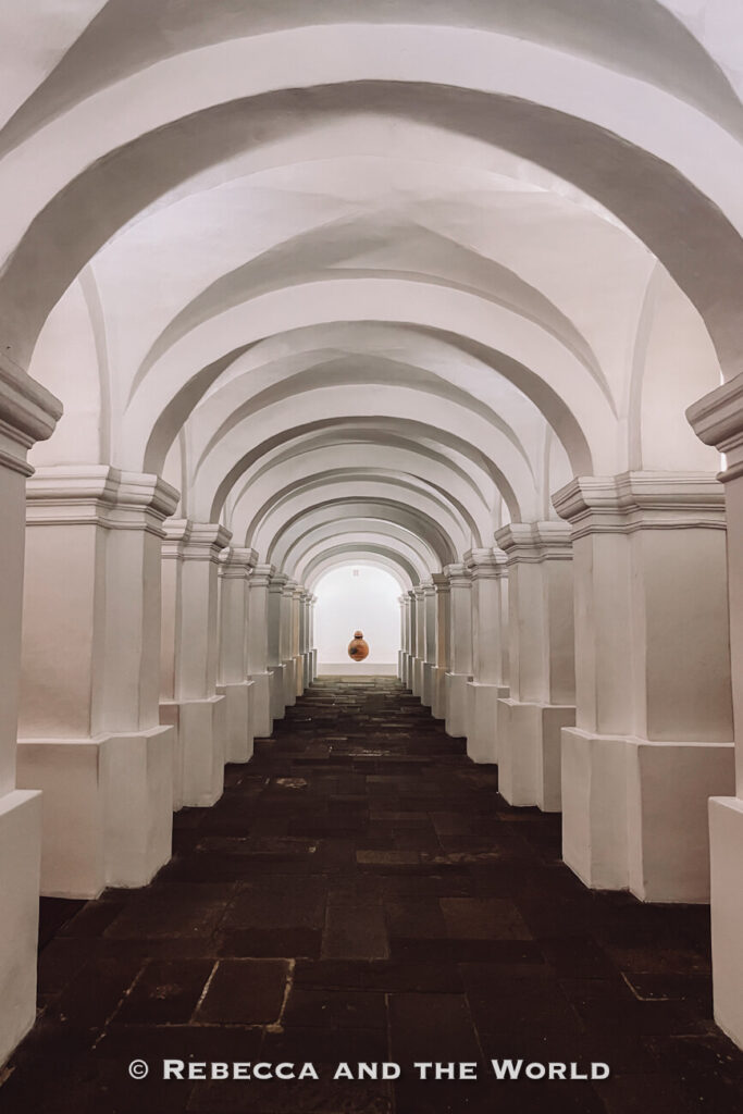 Long white arched corridor with repeating vaulted ceilings and dark stone floors leading to a ceramic vessel at the far end, photographed inside a historic museum - Museo Nacional de Colombia - during 2 days in Bogotá.
