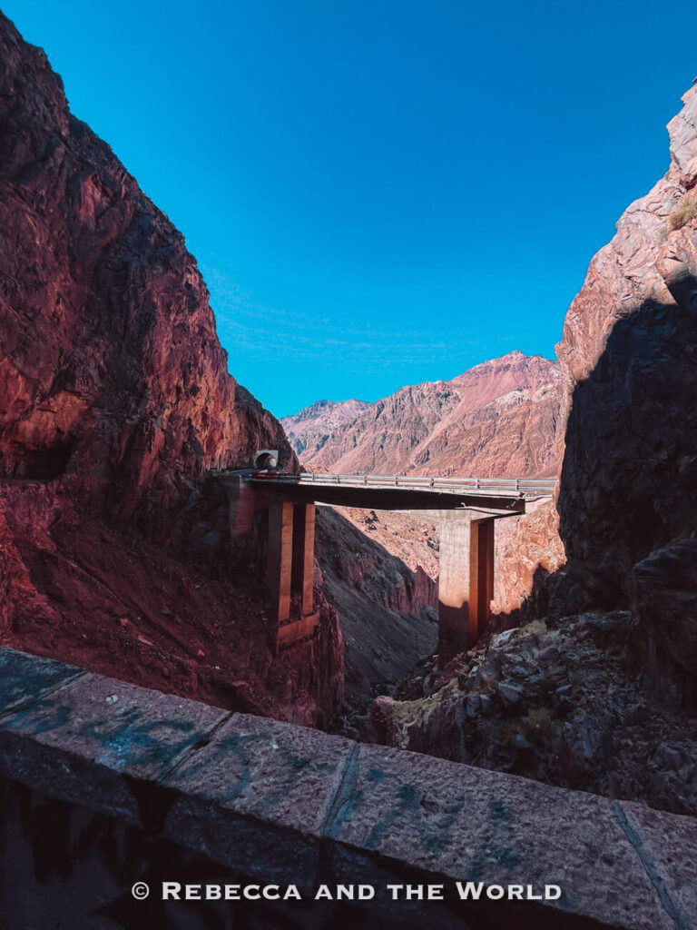 Concrete bridge crossing a narrow rocky canyon with steep cliff walls and a tunnel entrance under a clear blue sky. One of the striking things to do in Mendoza.