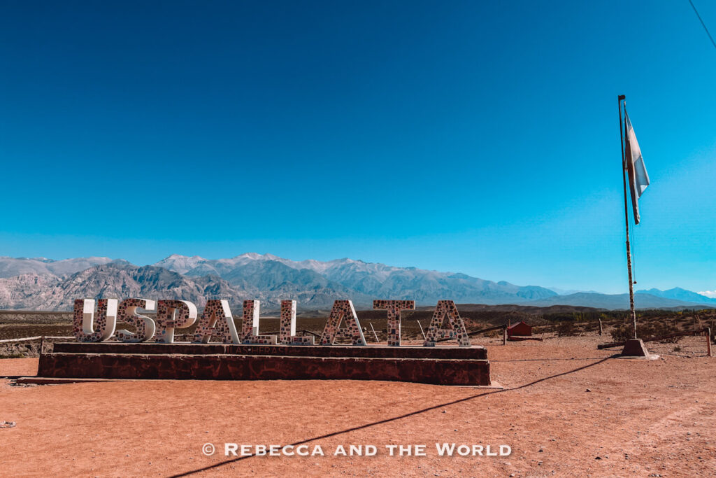 Large “Uspallata” sign standing in a dry mountain landscape with an Argentine flag and Andes mountains in the distance. Included in many 3 days in Mendoza plans.