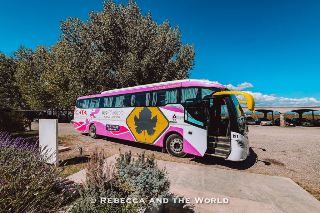 Colorful tour bus parked beside landscaped gardens and trees at a vineyard property. The Bus Vitivinicola is a convenient way to get around Mendoza.