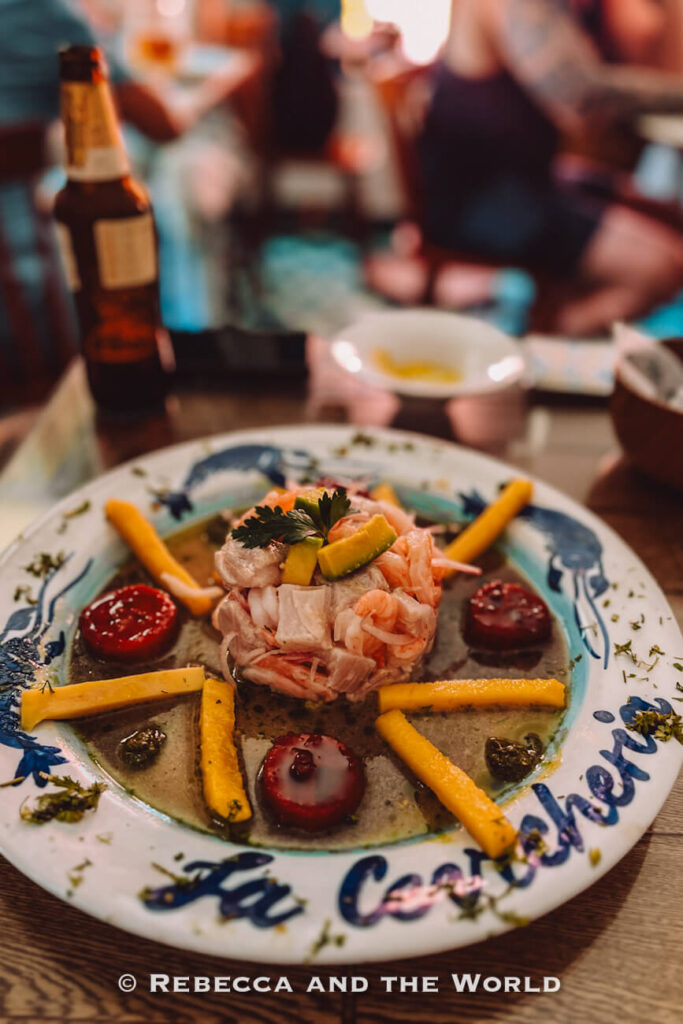 A plated ceviche dish topped with avocado and herbs sits in the center of a decorative plate, surrounded by sauces and garnishes. Trying local seafood is one of the best things to do in Cartagena.