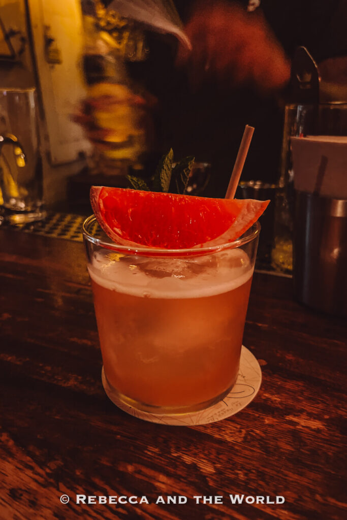 A pink cocktail with ice is served in a short glass and garnished with a grapefruit wedge, resting on a wooden bar counter. Enjoying craft cocktails is one of the popular things to do in Cartagena.