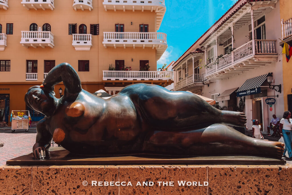 A large bronze sculpture of a reclining nude figure rests in a public square surrounded by colonial buildings with balconies, a landmark for anyone deciding what to do in Cartagena.