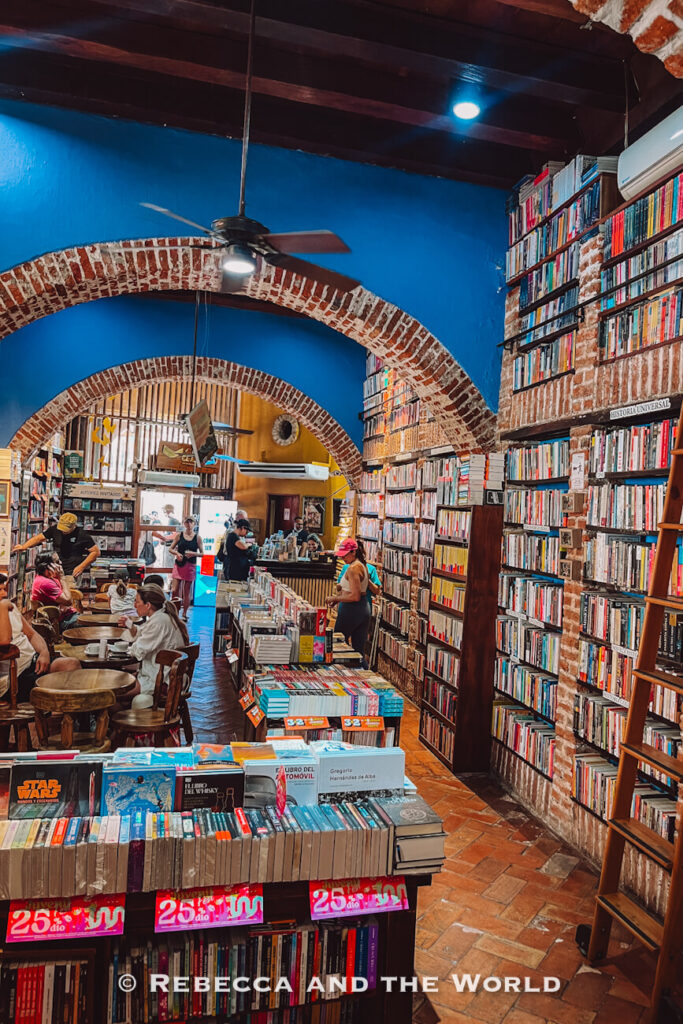 A bookstore interior has brick archways, tall shelves packed with books and people browsing or sitting at café tables, a cultural stop for a Cartagena itinerary.