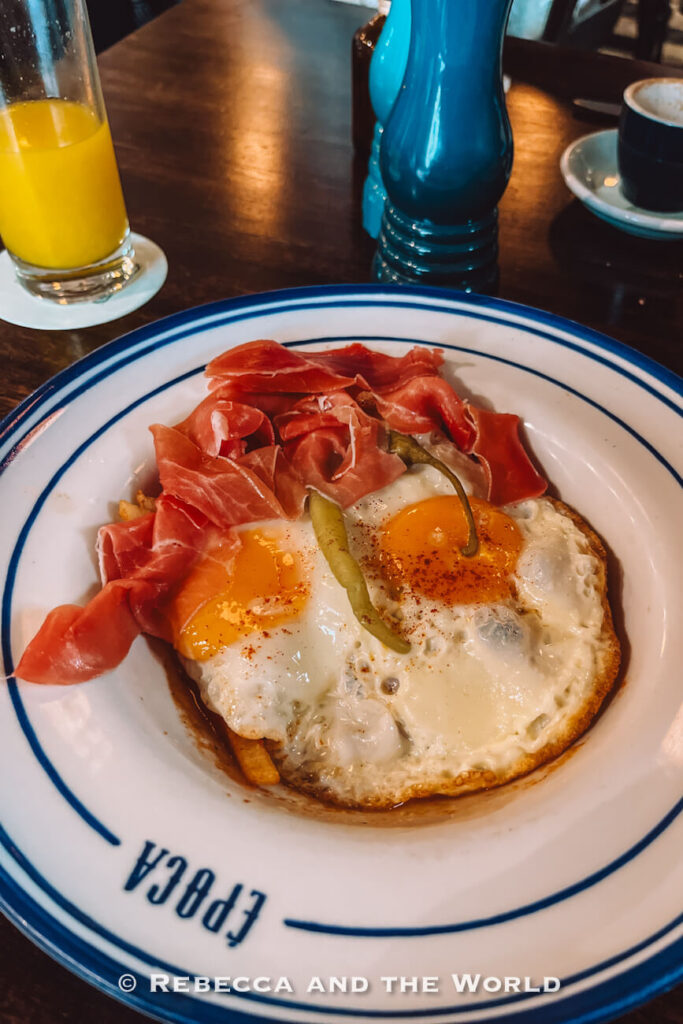 A plate of fried eggs topped with cured ham and a green pepper sits on a wooden table, part of a food-focused Cartagena travel guide.