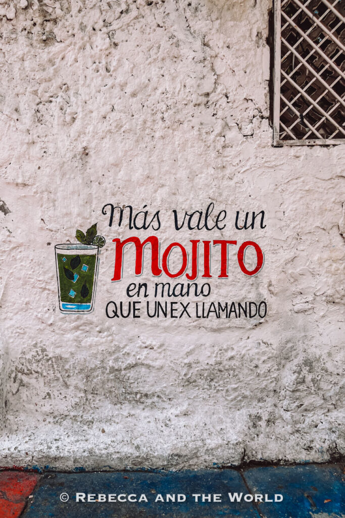 A painted wall sign reads “Más vale un mojito en mano que un ex llamando,” with a small mojito illustration, a playful detail in this Cartagena travel guide.