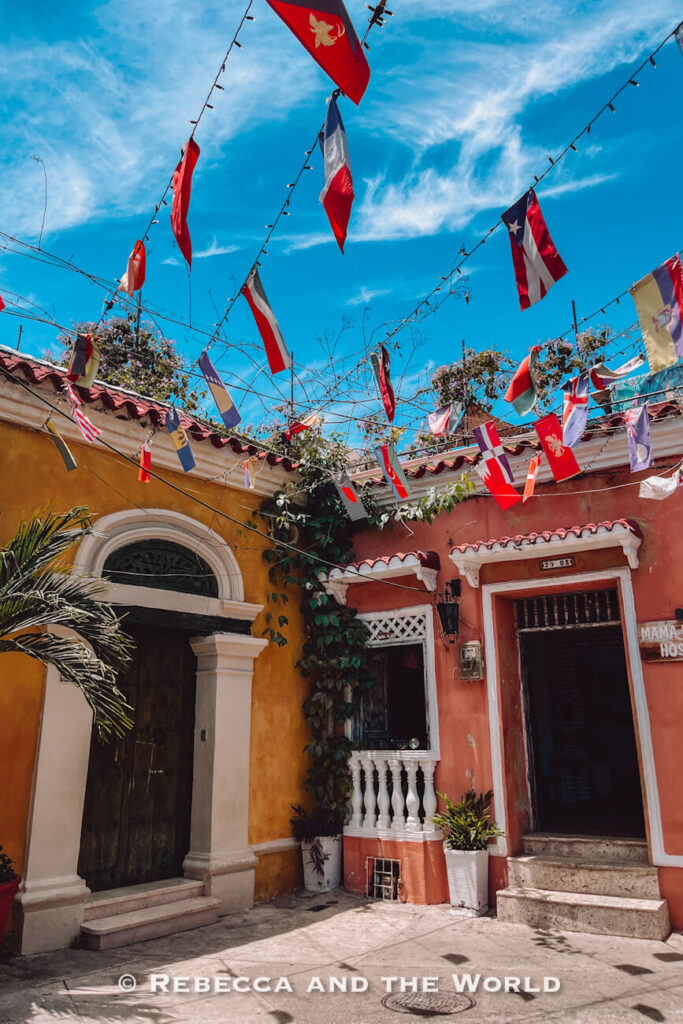 International flags hang above a sunny courtyard with yellow and coral colonial buildings, a colourful spot to see during 3 days in Cartagena.