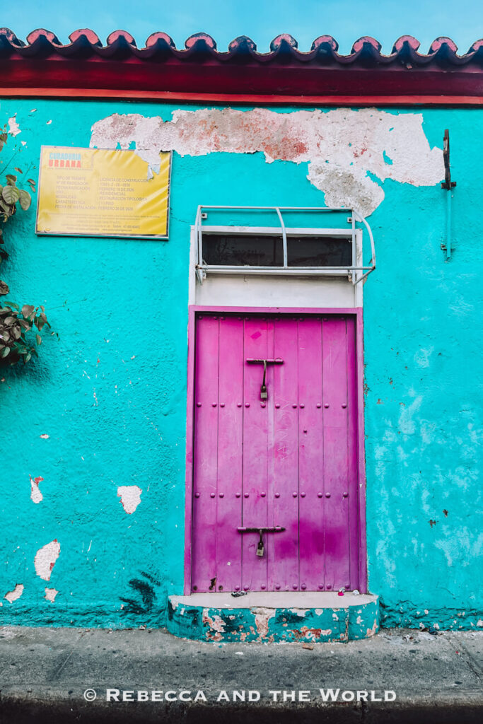A bright turquoise wall with a vibrant pink wooden door creates a colourful street scene, showcasing the bold architecture often featured in a Cartagena itinerary.