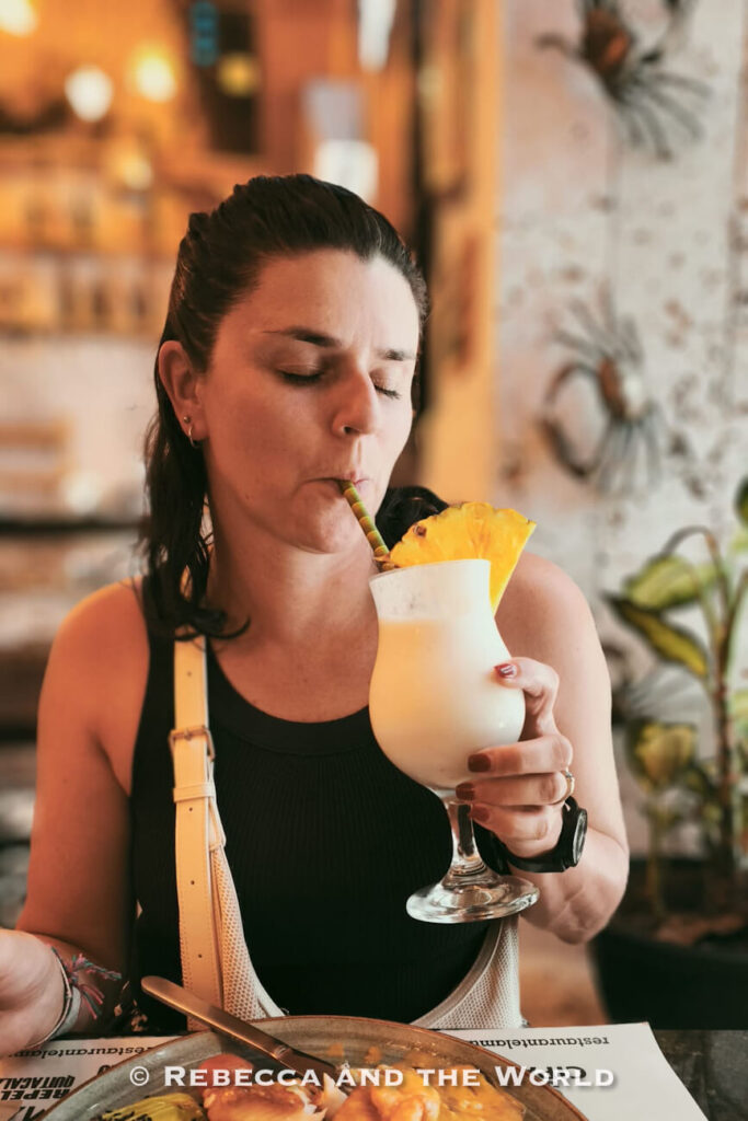 A woman - the author of this article - sits at a restaurant table sipping a creamy tropical cocktail garnished with a pineapple wedge, enjoying a meal during 3 days in Cartagena.