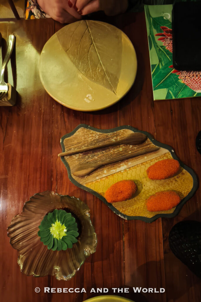 Several artistic dishes are arranged on a wooden table, including three croquettes on a decorative serving platter and a flower-shaped green dessert on a sculptural plate. Dining at innovative restaurants is a popular answer to what to do in Cartagena.