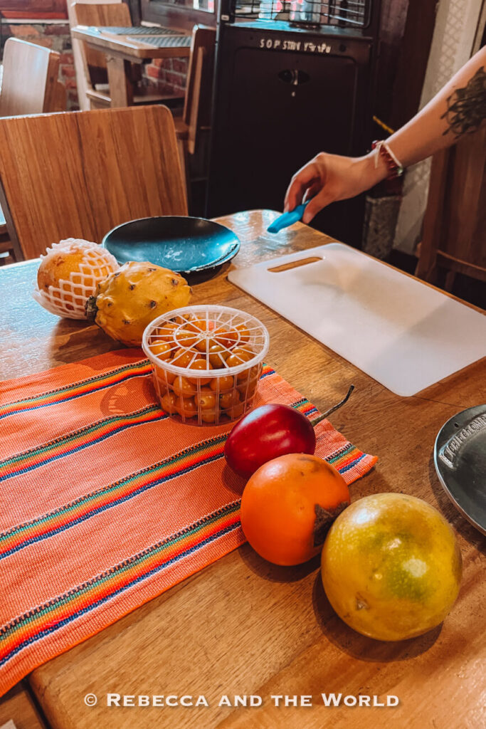 Wooden table set with tropical fruits, including passion fruit, dragon fruit, small orange berries, and tree tomato, showing ingredients in Colombian dishes.