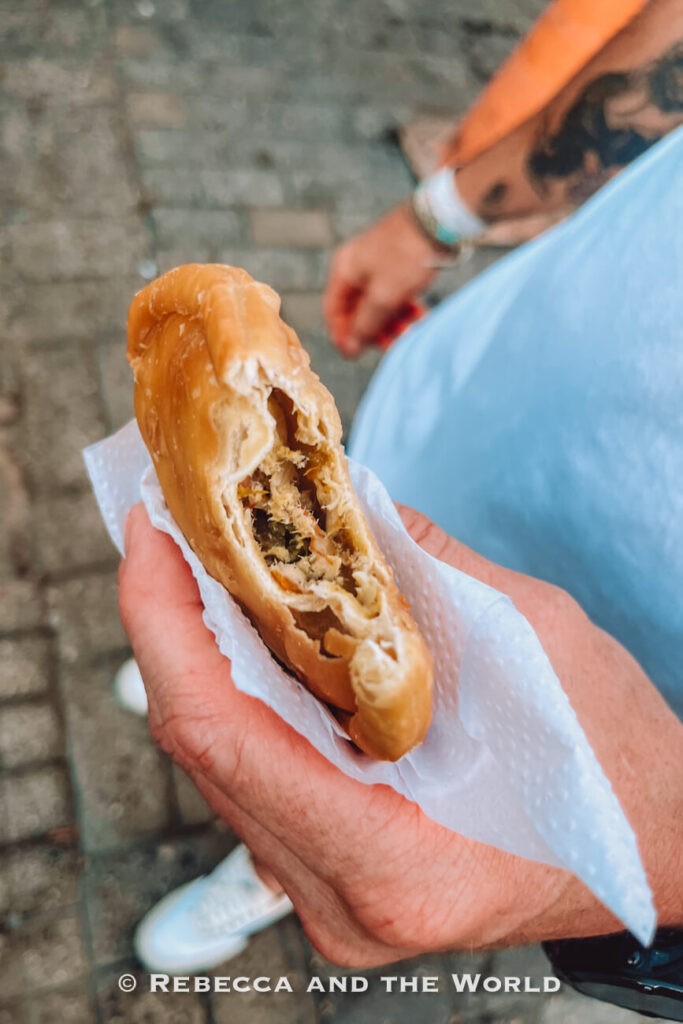 A hand holds a partially eaten fried chicken empanada with savory filling wrapped in a napkin while standing on a cobblestone street during a Cartagena street food tour.