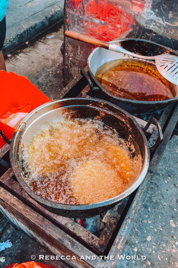 Two metal pots of hot oil bubble on a roadside cooking station with frying utensils resting on the edges during a Cartagena food tour.