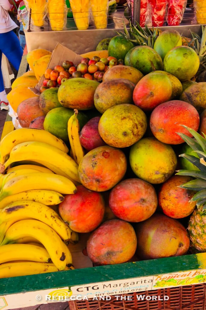 A colorful fruit stand piled high with bananas, mangoes, pineapples, papayas, and other tropical fruit at an outdoor market featuring street food in Cartagena.