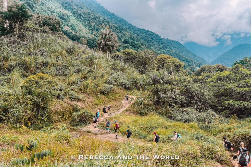 Group of hikers walking along a dirt trail through green mountains and tropical vegetation during the Lost City trek in Colombia.