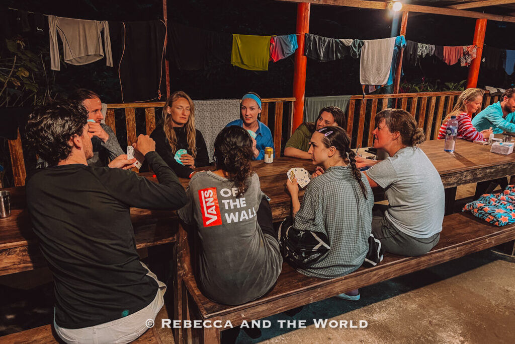 Travelers playing cards around a wooden table at a jungle campsite during an overnight stop on the Ciudad Perdida hike.